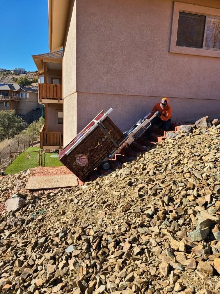 Crew moving a large safe down outdoor stairs with a powered stair-climbing dolly.