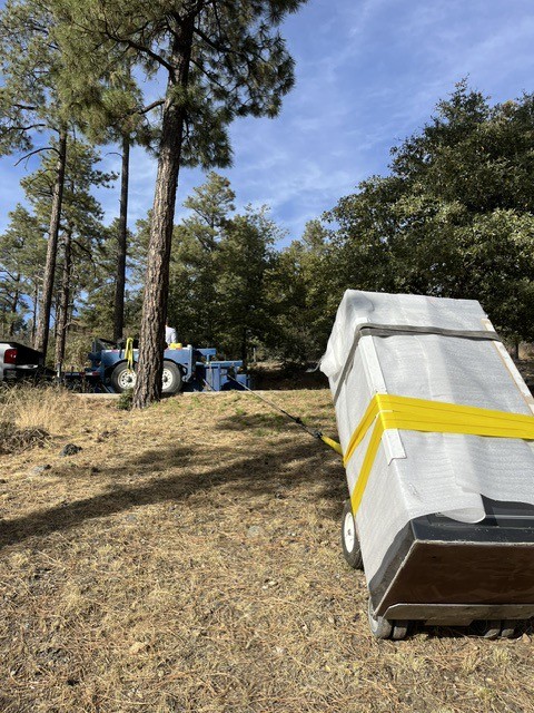 Wrapped safe on a wheeled cart, towed across a pine hillside.