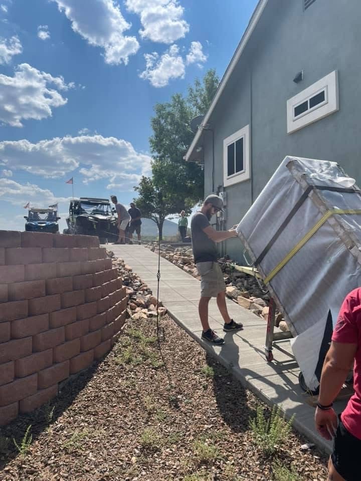 Crew rolling a blanketed safe along a house walkway on a heavy dolly.