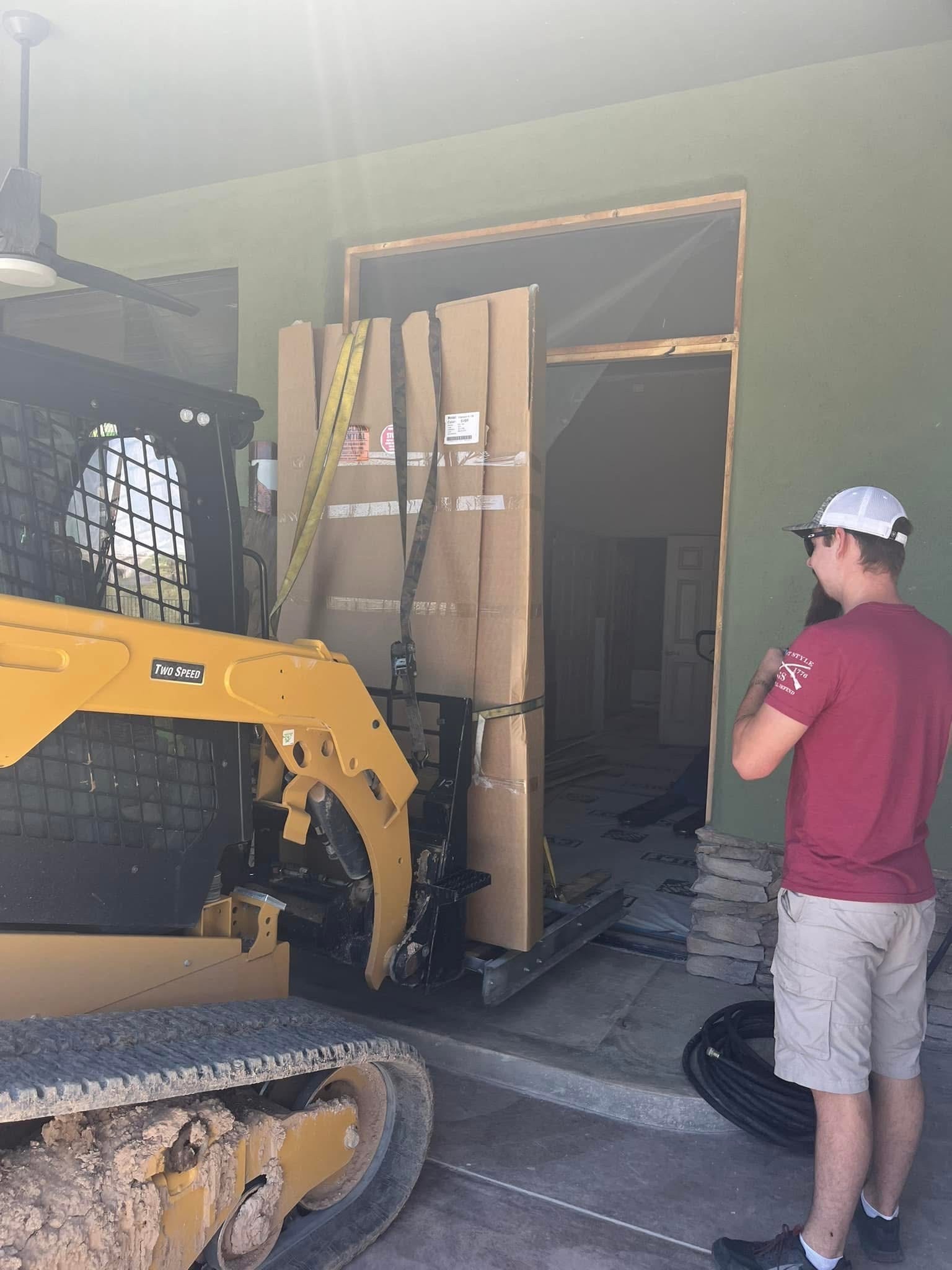 Crated safe lifted by a compact track loader through a framed doorway.