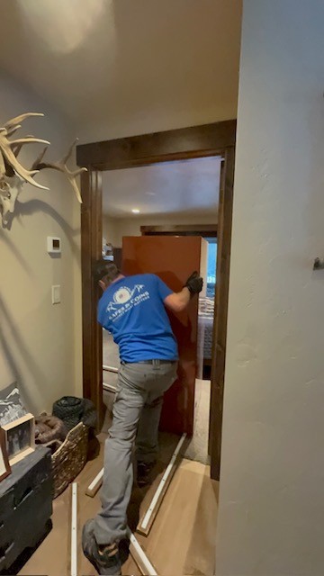 Crew in a Mountain Pass Safes shirt moving a safe through a doorway on floor runners.