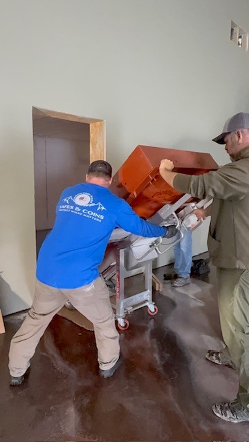 Crew in a branded shirt moving a copper-colored safe through a doorway.